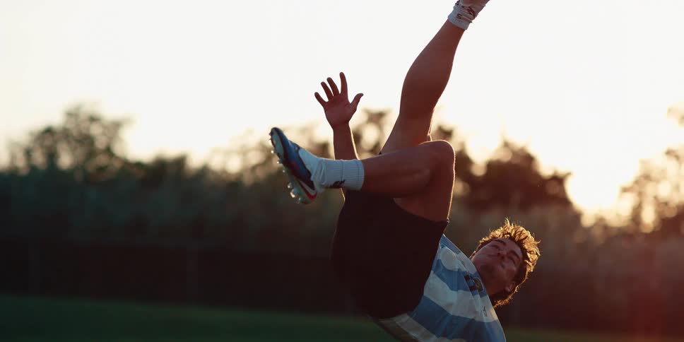 Man uses a bicycle kick to send the soccer ball through the air in summer near sunset