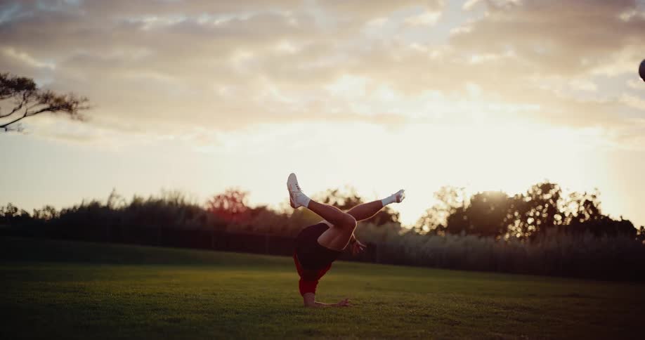 A male soccer player performs a bicycle kick on a grassy field at sunset