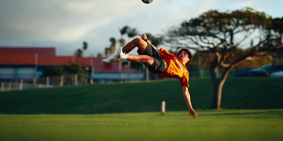 A man performs a bicycle kick with a soccer ball on a grass field