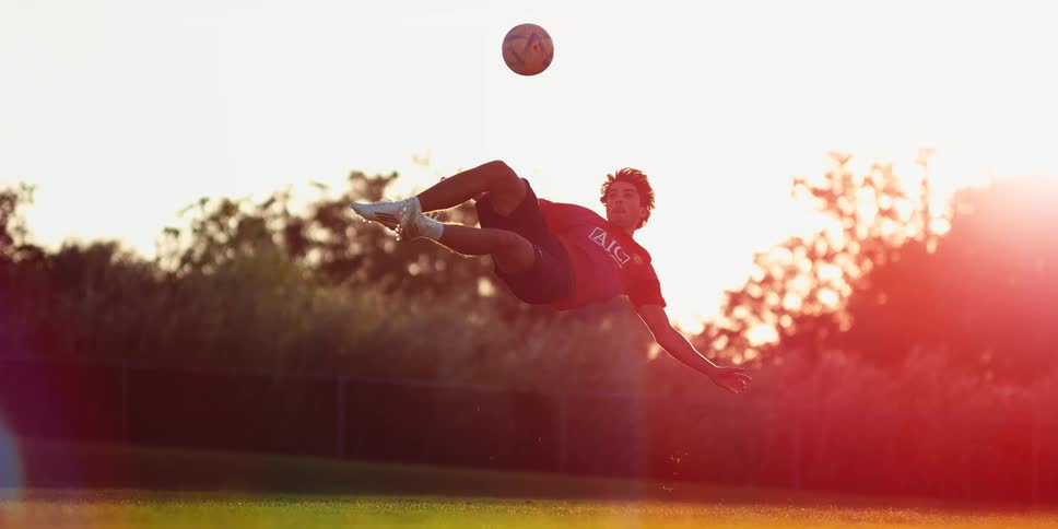 Player performing a bicycle kick to strike a soccer ball during a match on a grass field