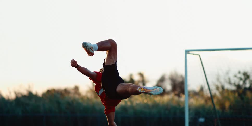 A male soccer player performs a bicycle kick on a grass field in slow motion