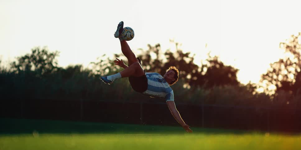 Player performing a bicycle kick to strike a soccer ball on a grass field