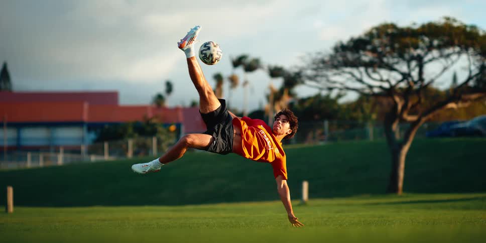 A soccer player performing a bicycle kick while striking a ball on a grassy field