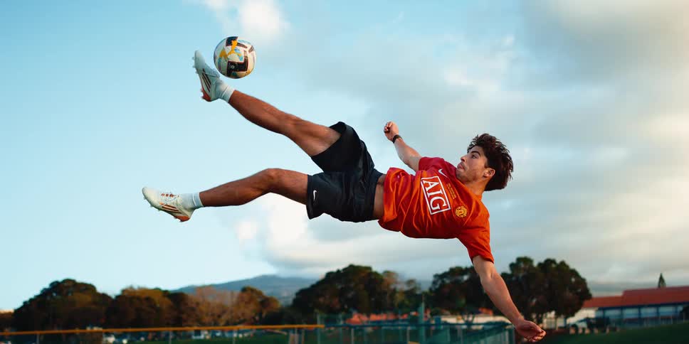 Player performing a bicycle kick to reach a soccer ball in the air on an open field