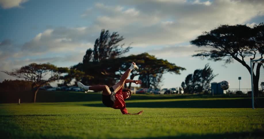 A football player performing a bicycle kick on the field kicking a soccer ball at midday
