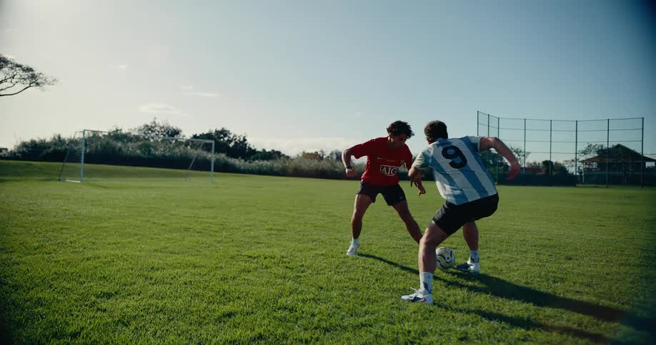 Two young men play one on one soccer on a soccer field at the park on a summer day