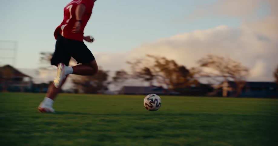 Player running toward a soccer ball on a grass field with a goal in the background