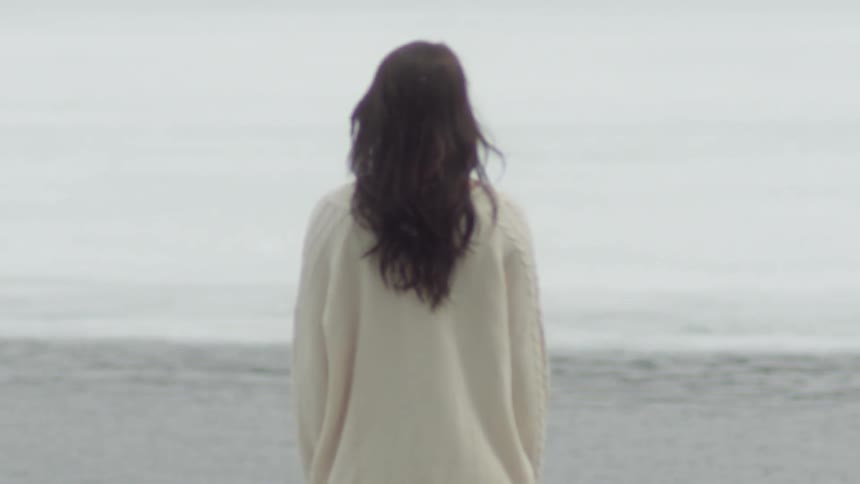 A woman stands watching the ripples on the water