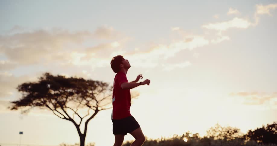 Soccer player standing in a field bouncing a soccer ball into the air with his feet and it rolls away