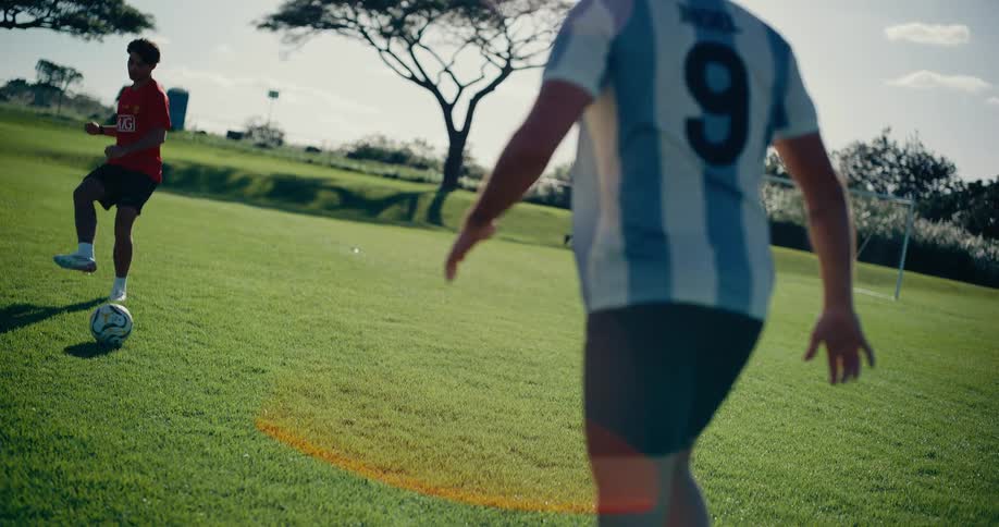 Two sportsmen pass and control a soccer ball while playing together on a grassy field at sunset