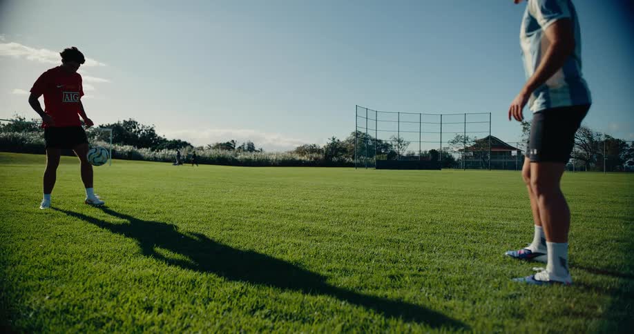 Two soccer players stand on the field kicking the ball back and forth to each other