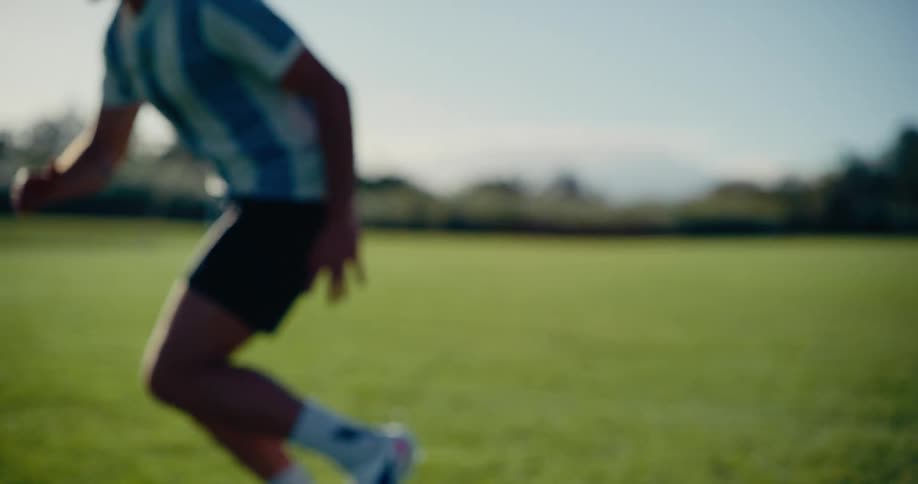 A soccer player in a red jersey dribbles a ball across a sunny grass field before the camera pans to follow a second athlete wearing a light blue striped kit with the number nine on his back as he runs toward a distant tree