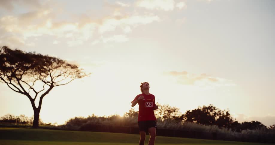 A football player juggling the ball on a field at sunset