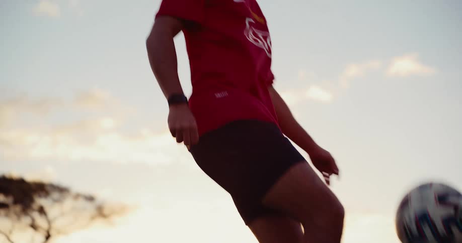 Players legs performing keepieups with a soccer ball on a grass field at sunset