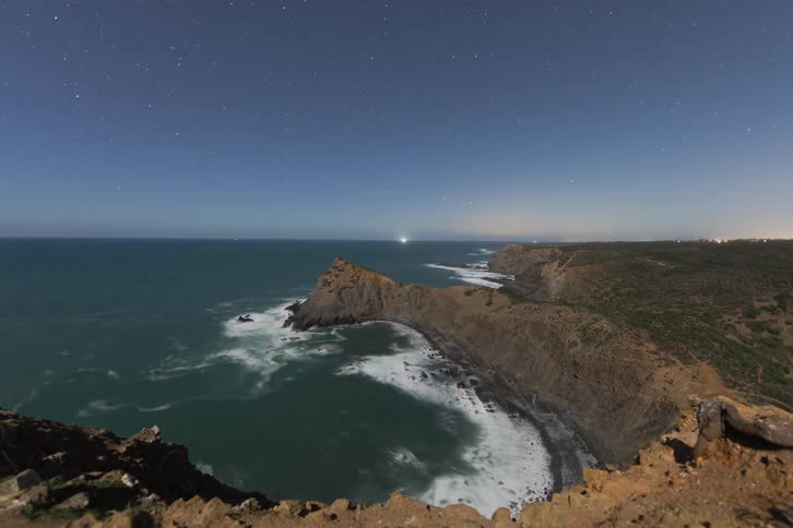 Dawn over coastal cliffs with ocean and starry sky on the horizon
