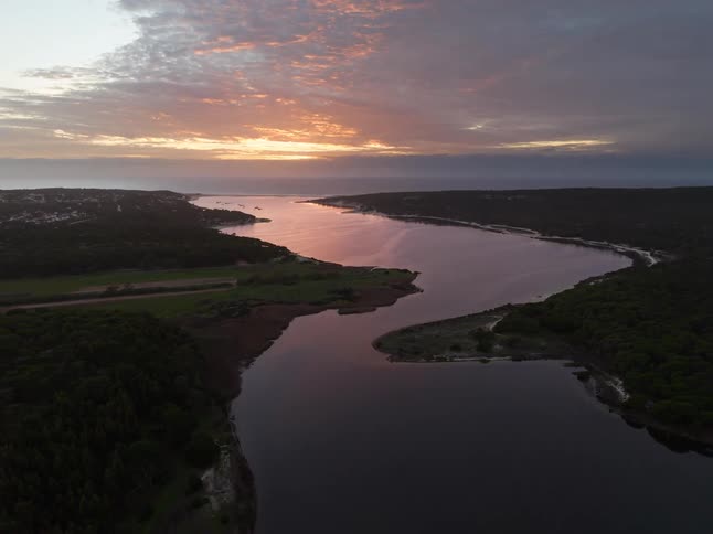 River passing a town and the rural wilderness reflects the sunlight as the setting sun tints the sky and the clouds