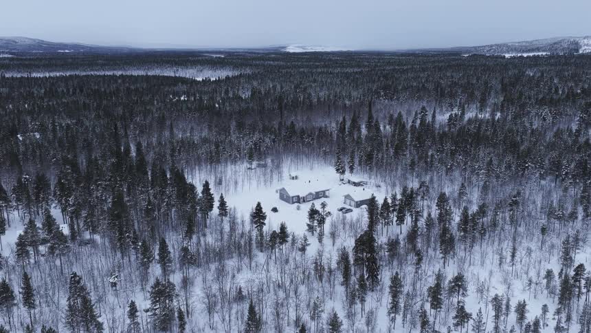 An aerial view shows a small cluster of buildings nestled in a vast snowcovered forest during a gloomy daythe surrounding landscape is dominated by dense frostcovered trees that stretch toward distant hazy hills under an overcast sky