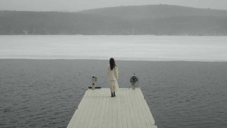 Woman wearing white walks out on a white dock towards the water