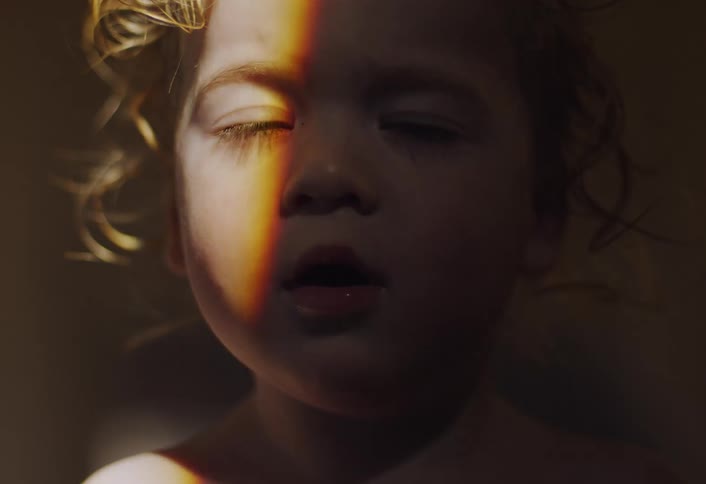 A young curly haired child up close looking ahead as a ray of light scans over the child