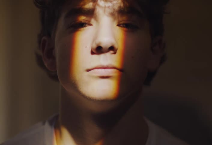A young boy is looking fowardin a dimly lit room with a ray of light scanning over his face