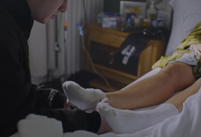 A man putting socks onto a woman in the hospital