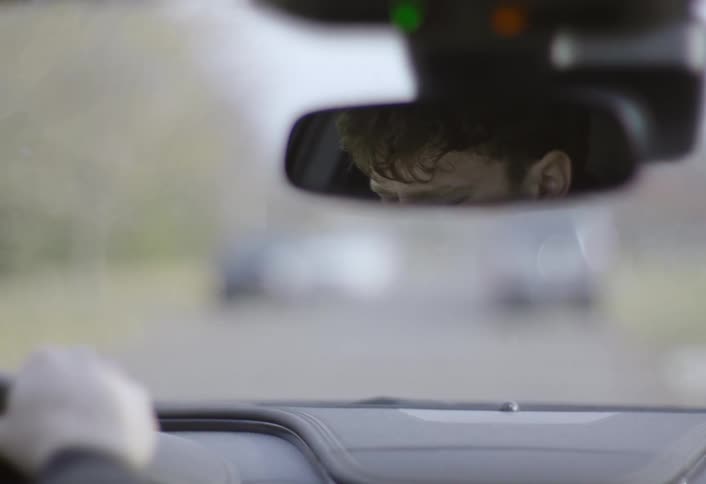Man drives a car with his head tilted down and hand on the steering wheel