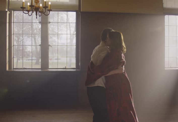 A young couple dances slowly together in a dimly lit sunlit bedroom