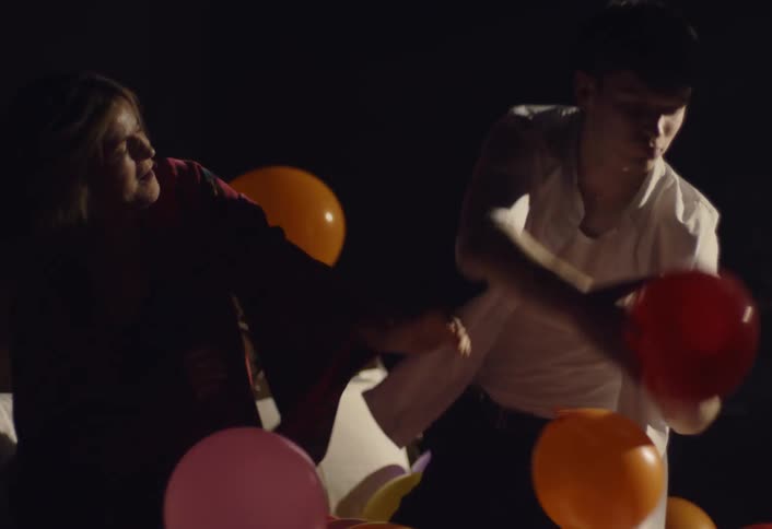 Woman and a man dance while playing with balloons in a darkened bedroom