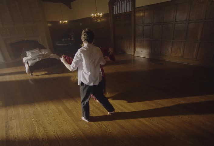 Couple dances in the center of a large hall with a wooden floor