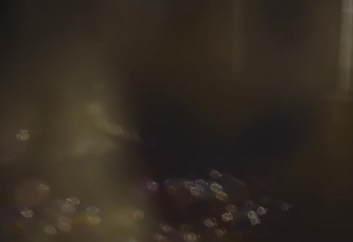 A macro shot of a golden antique clock face transitions into a hazy view of a person dancing in a dark room filled with colorful balloons on the floor