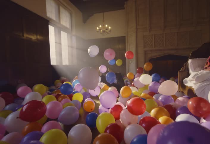 A man dancing passionately in a bright room with colorful balloons as sunlight streams through large windows