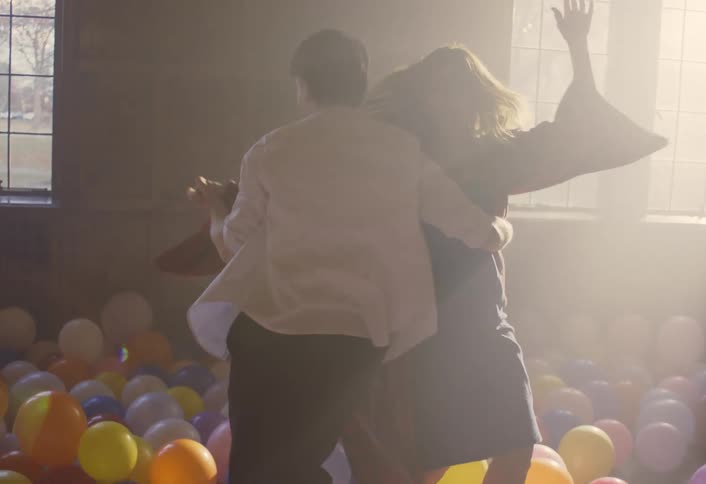 Man spins a woman while they dance among colorful balloons on the floor