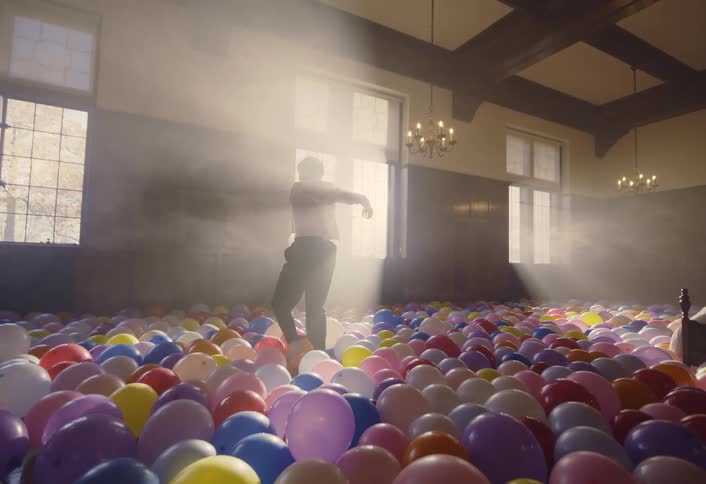 Man dances among colorful balloons scattered across the hall