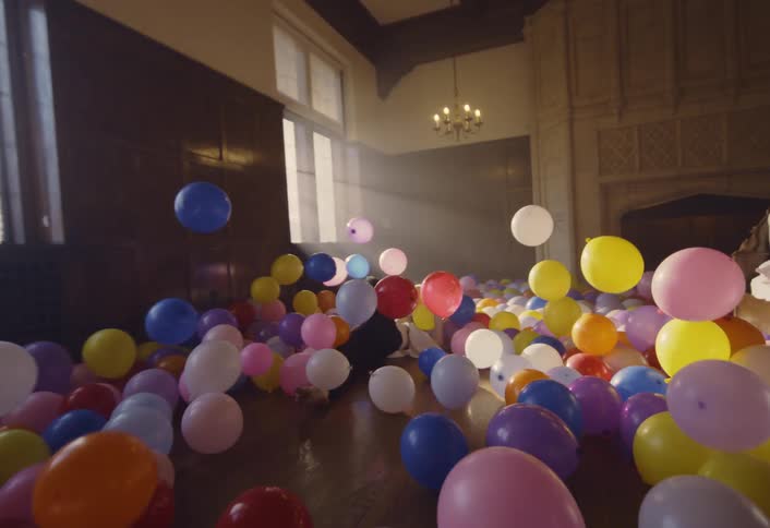 A man dances and spins before diving into a pile of balloons covering the floor