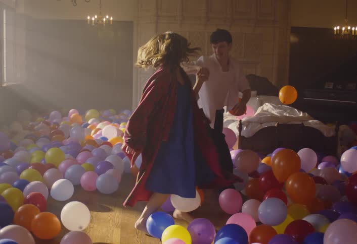 A man and woman playfully dance in a room filled with balloons