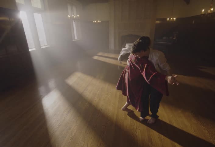 Young man and woman dance together on a wood floor with sunlight shining brightly in the windows