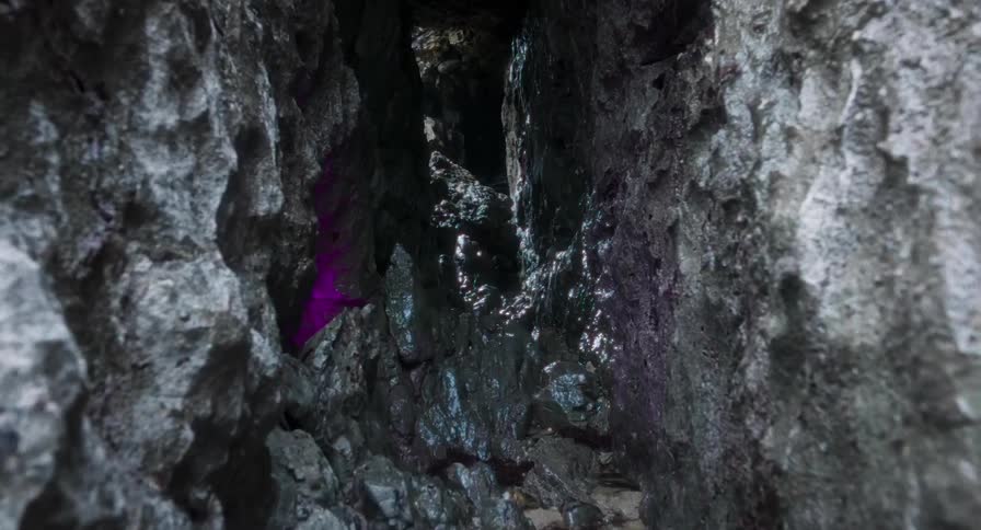 A narrow wet rock crevice inside a dark cave with water trickling through the rugged stone passage