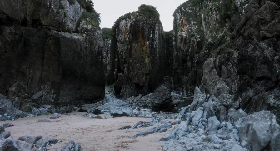 Tall gray cliffs that are covered in vegetation overlook a sandy beach