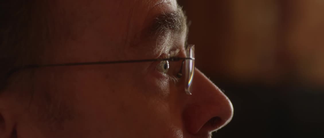 A man wearing glasses blinks and stares ahead