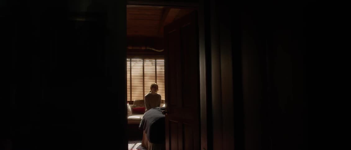 A woman is sitting on a bed down the hall