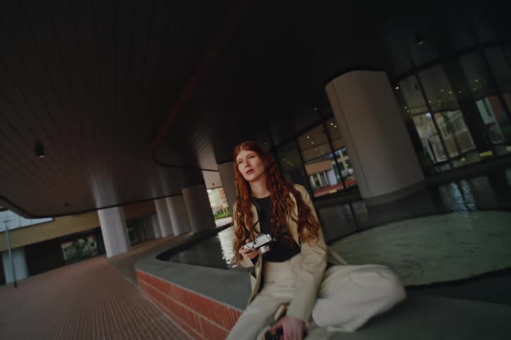 Young woman holds her camera taking a picture as she sits outside of a mall