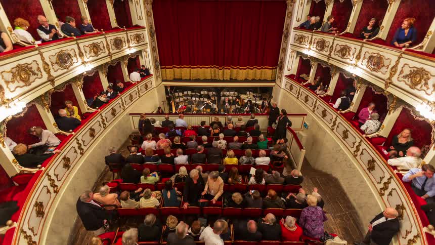 Audience watches an orchestra perform in a theater with side balconies