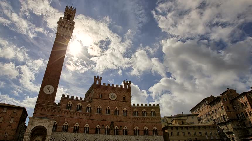 Historic tower and brick building illuminated by sunlight under a cloudy sky