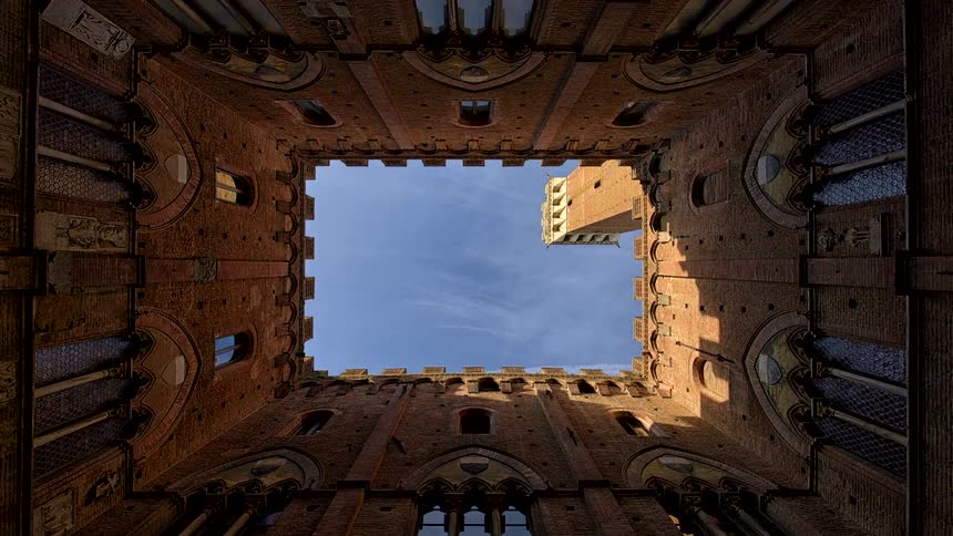 View from the palazzo pubblico courtyard looking up at the sky as sunlight shines on the torre del mangia tower