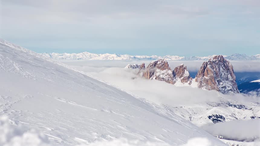 Low lying clouds pass a snow covered slope in the mountains on a winter day