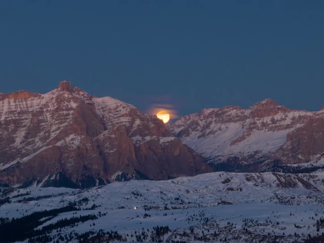 Moon rises between snowcovered mountains at dusk