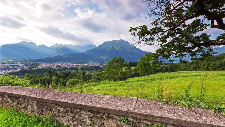 A wide landscape view of a mountain range overlooking a valley town with a stone wall in the foreground
