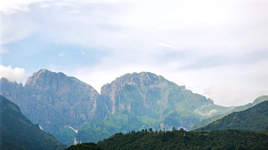 Forested mountains and clouds moving over the rough terrain of rocky mountains