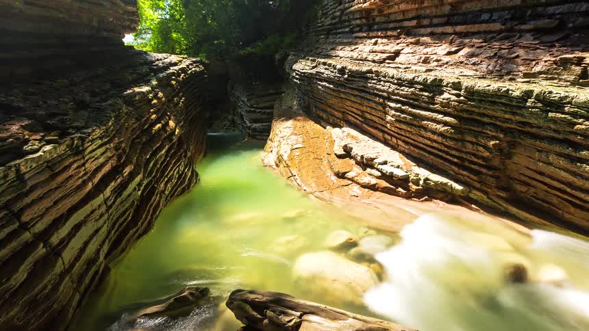 Sunlight shines on the ridges of a cliff as water in a stream flows through the gorge