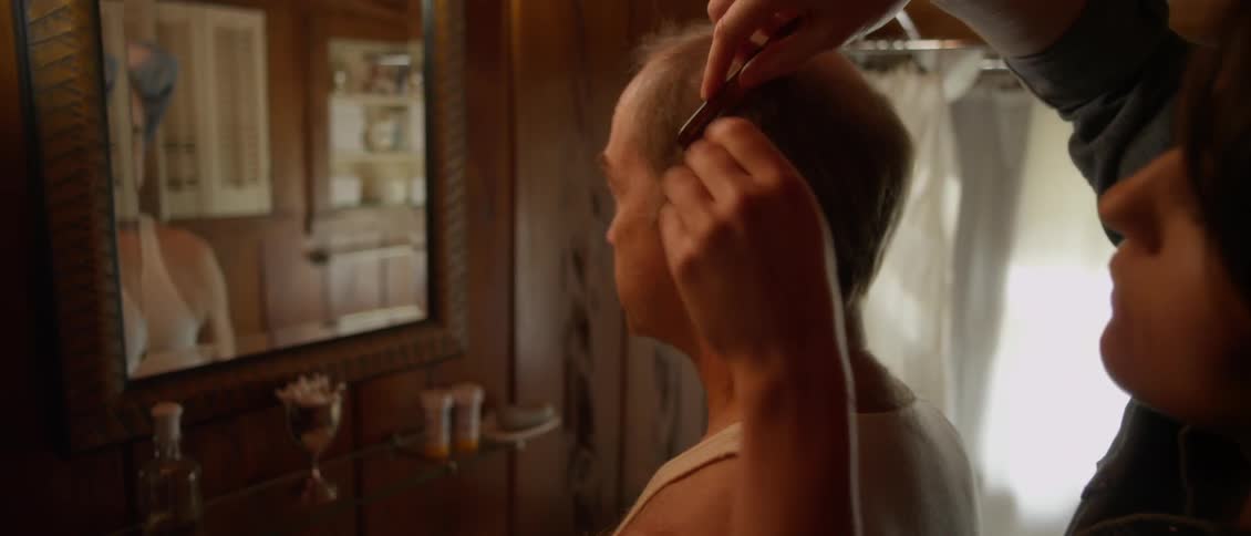 A man is having his hair combed in front of a mirror